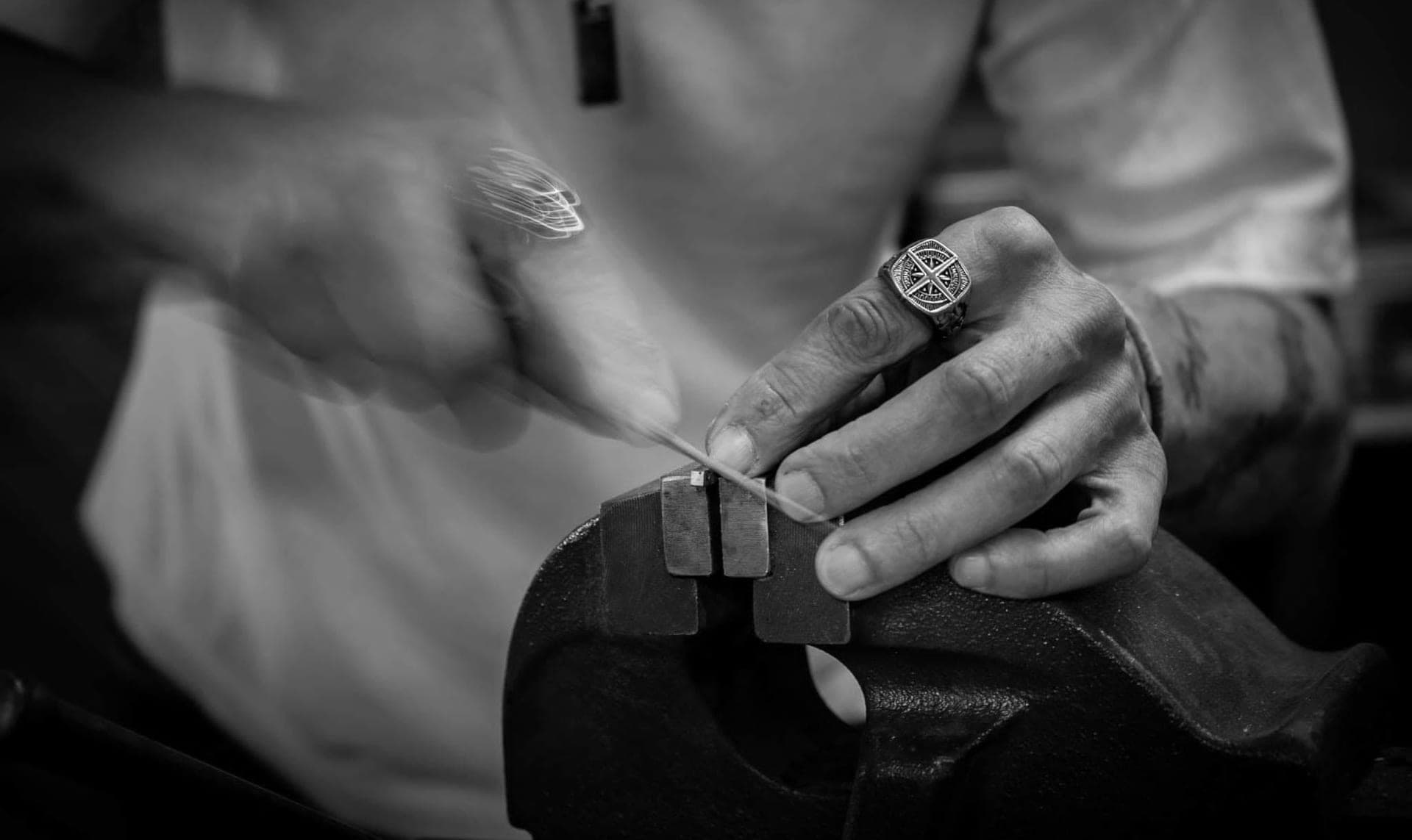 Travail de précision à l'étau dans l'atelier du Résiliant : les mains du coutelier ajustent une pièce, photo en noir et blanc.